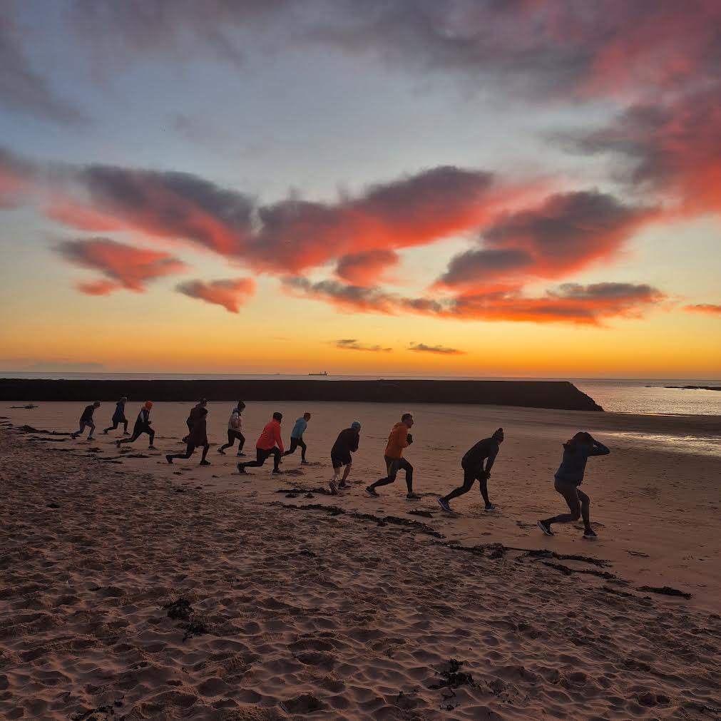 Group sprinting up the beach at sunrise